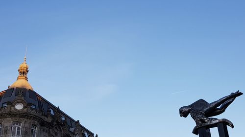 Low angle view of statue against building against clear blue sky