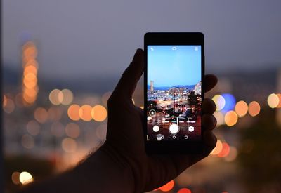 Cropped image of person photographing illuminated smart phone at dusk