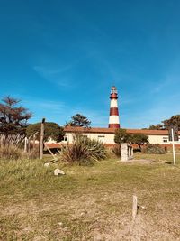 Lighthouse on field by buildings against blue sky