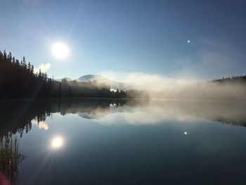 Scenic view of lake against bright sun in sky