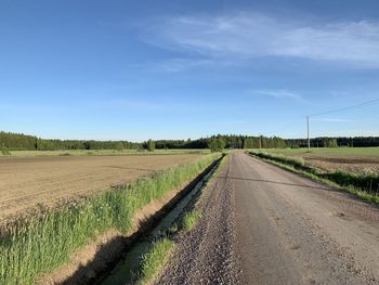 Empty road amidst agricultural field against sky