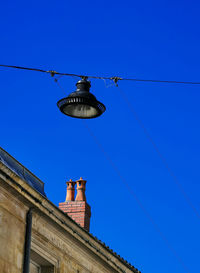 Partial view of a house with fireplace and street light against blue sky.