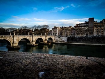 Bridge over river by buildings against sky