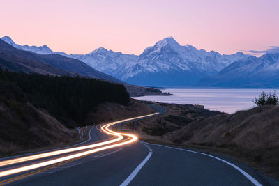 Road amidst snowcapped mountains against sky during sunset