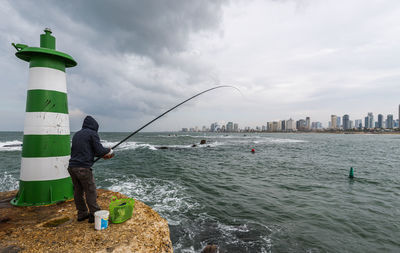 Man fishing in sea against sky