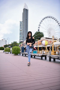 Full length portrait of woman standing in city against sky