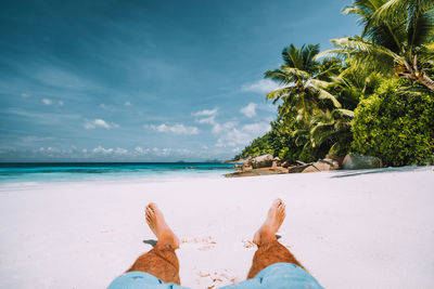 Low section of man sitting at beach against blue sky