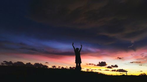 Silhouette man standing on field against dramatic sky at sunset