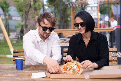A married couple in a street restaurant drinking coffee and eating pizza