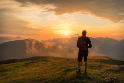 Rear view of man standing on mountain against sky during sunset