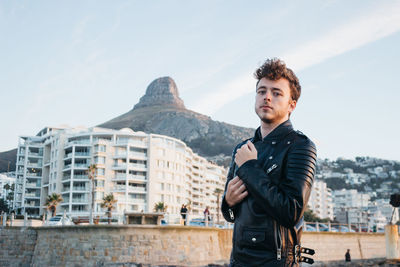 Portrait of young man standing in city against sky