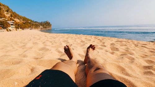 Low section of person on beach against sky