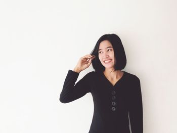 Smiling young woman looking away while standing against white background