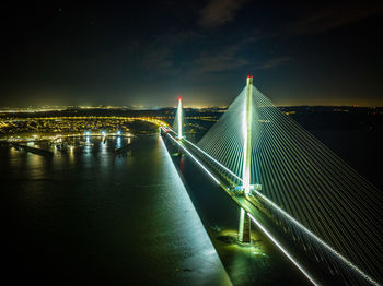 Illuminated bridge over river against sky at night