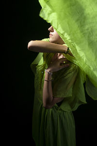 Close-up of young woman holding plant against black background