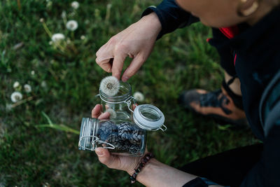 Close-up of man holding dandelion with pine cones in jar outdoors