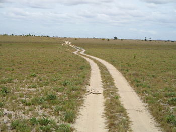 Dirt road amidst field against sky