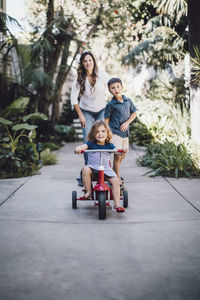 Daughter riding tricycle while mother and brother standing in background