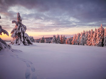 Snow covered landscape against sky during sunset