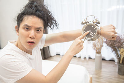 Portrait of man showing alarm clock at home