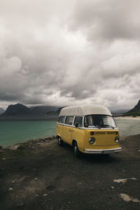 Yellow car on road by sea against sky