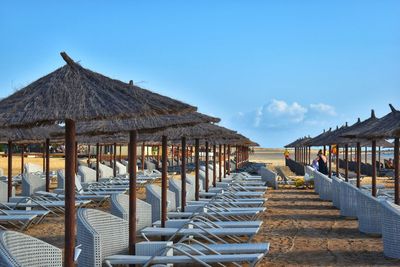 Empty chairs and tables at beach against blue sky