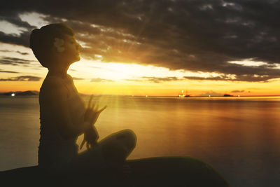 Silhouette man sitting by sea against sky during sunset