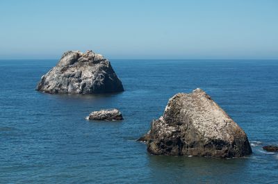 Rocks in sea against clear blue sky