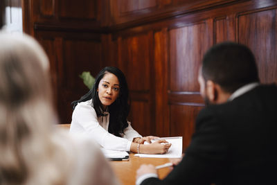 Confident businesswoman discussing over contract document with colleagues in board room