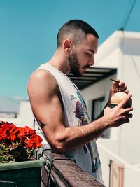 Young man holding flower while standing by railing