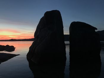 Silhouette rocks by sea against sky during sunset