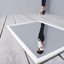 Low section of mid adult woman reflecting on mirror while standing at hardwood floor