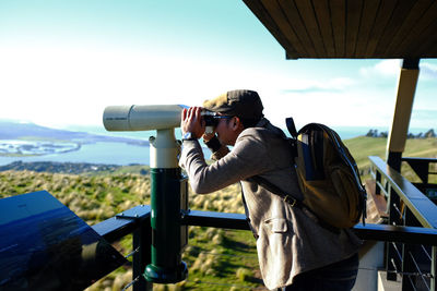 Side view of man looking at camera against sky