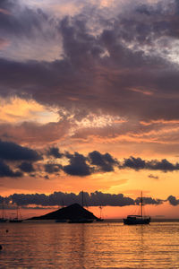 Silhouette of boats in sea against cloudy sky