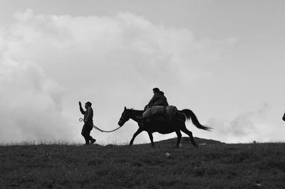 Low angle view of man walking by woman riding horse on land