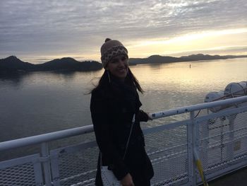 Young woman standing by railing against lake during sunset