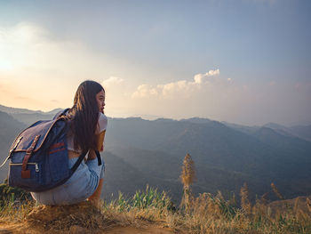 Backside of woman with backpack sitting to enjoy on mountains peak in the morning