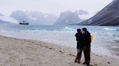 Full length of couple kissing while standing by frozen lake during winter