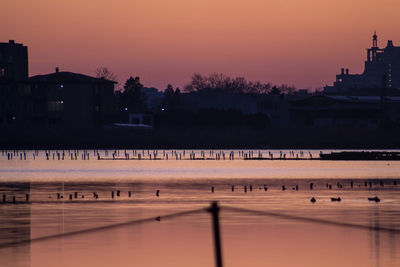 Scenic view of river by silhouette buildings against sky at sunset