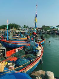 Fishing boats moored at harbor against clear sky