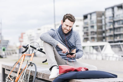 Businessman in the city with bicycle using smartphone and earphones