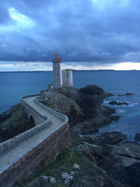 Lighthouse on calm sea against cloudy sky