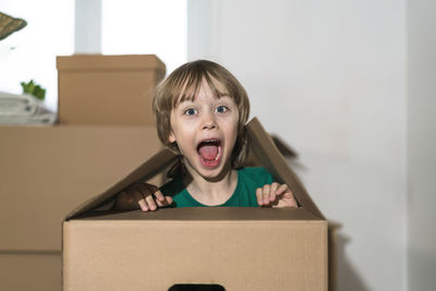 Cute toddler boy playing in cardboard box at new home.