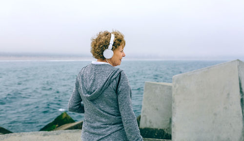 Senior woman standing on pier at beach against sky