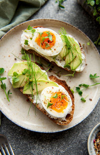 Bread toast, boiled eggs, avocado slice, microgreens on a plate, breakfast time