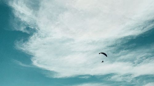 Low angle view of people paragliding against sky