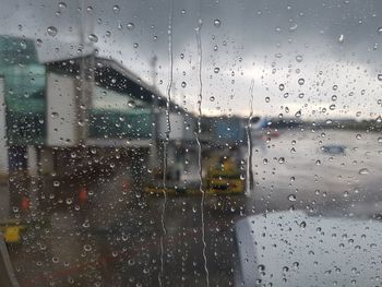 Buildings against cloudy sky seen through wet window