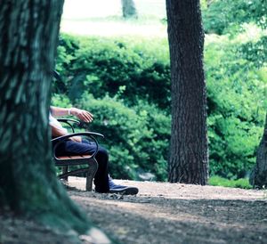Low section of man sitting on bench at landscape