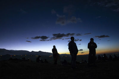 Silhouette people standing on field against sky at dusk