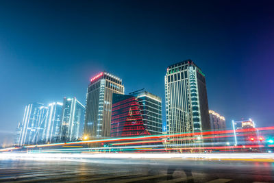 Light trails on city buildings against blue sky at night